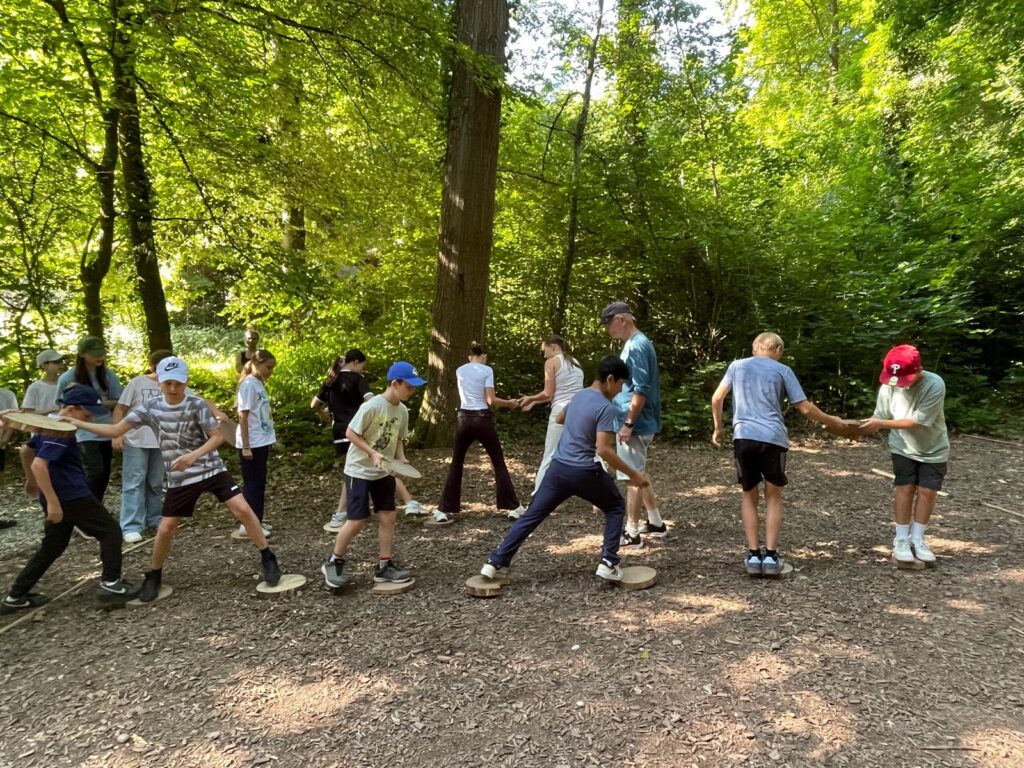 260619ExkursionWaldhaus1 Schüler machen Teambuildingaufgaben im Wald - Balancieren auf Holzscheiben