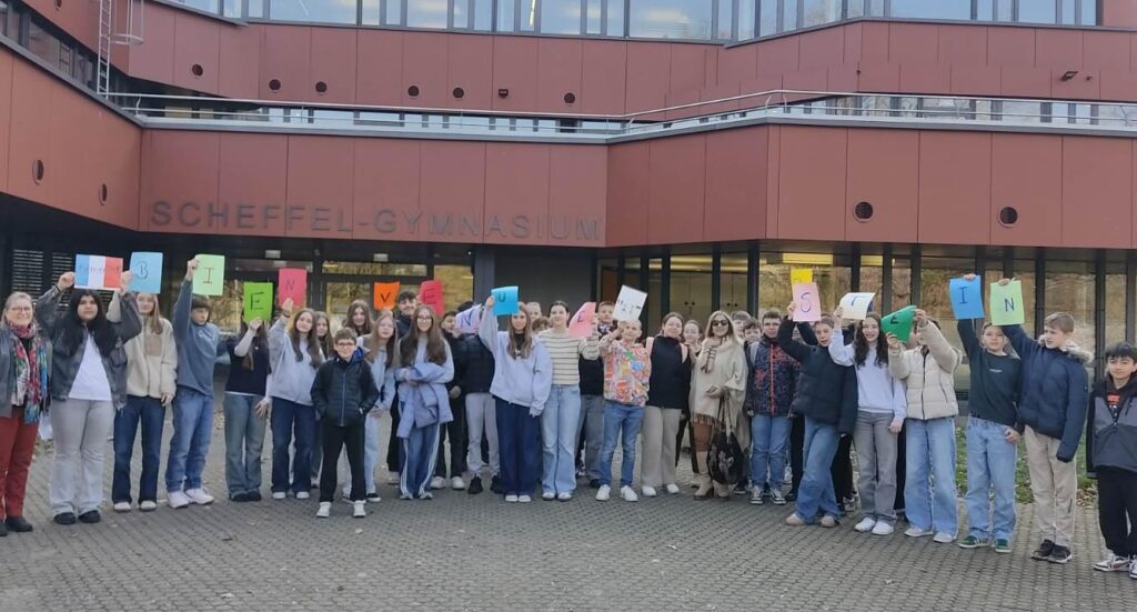 Französicshe und deutsche Schülerinnen und SChüler vor dem Scheffel-Gymnasium halten Buchstaben mit Bien venu Erstein in die Höhe