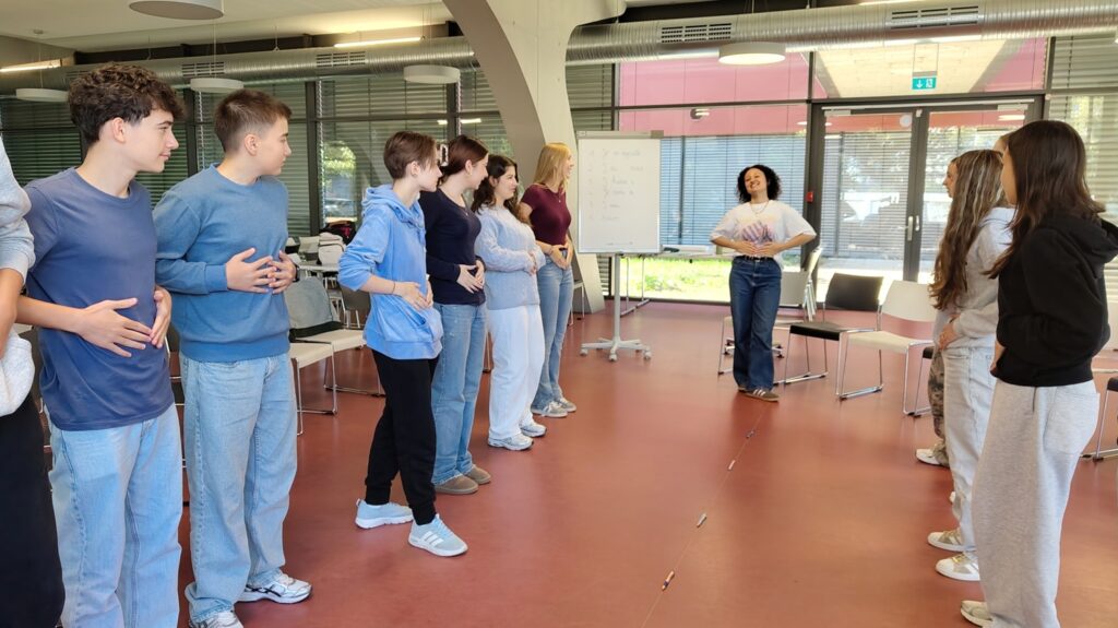 Schüler:innen werden von Lektorin Léa zum Körperteile-Reaktionsspiel angeleitet